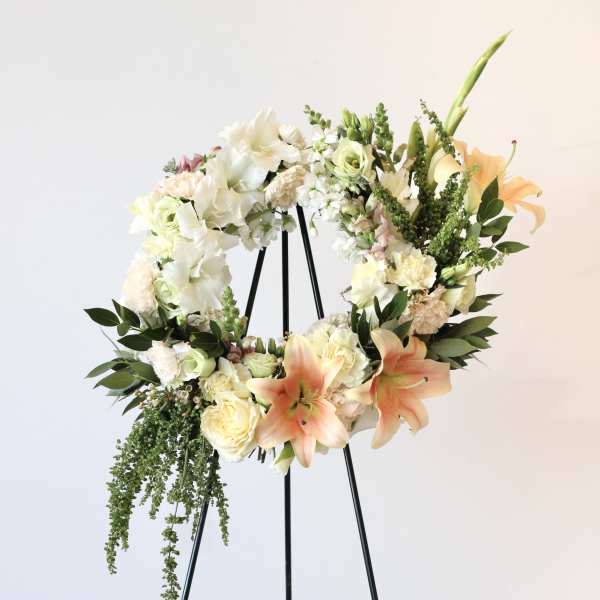 Floral wreath on a black stand with white, peach, and green blooms