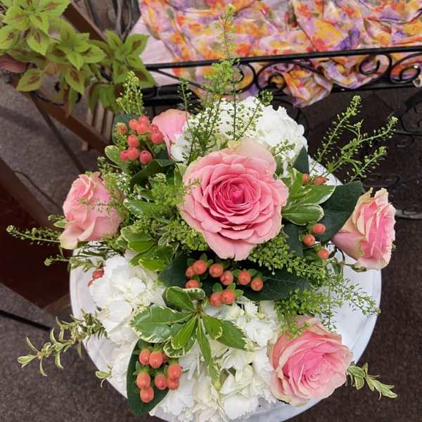 Round arrangement of pink roses with white hydrangeas and peach berries viewed from above.