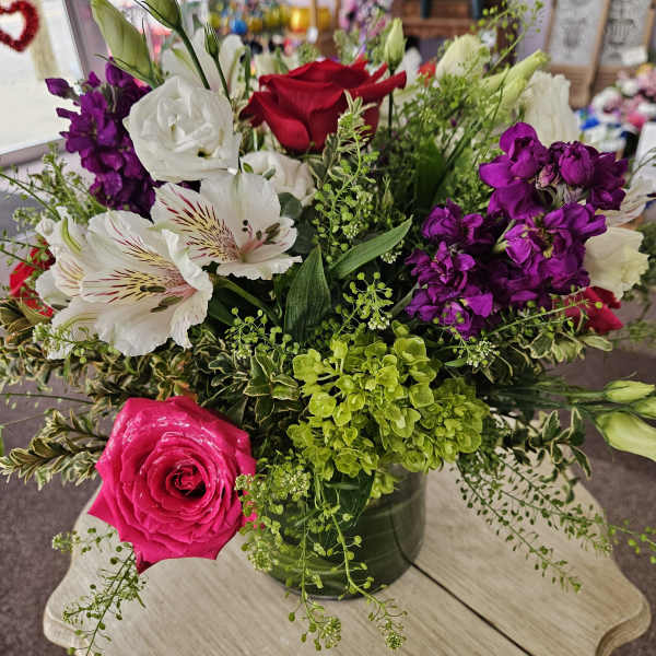 Mixed bouquet of pink and red roses, white blooms, and purple flowers in a clear glass vase