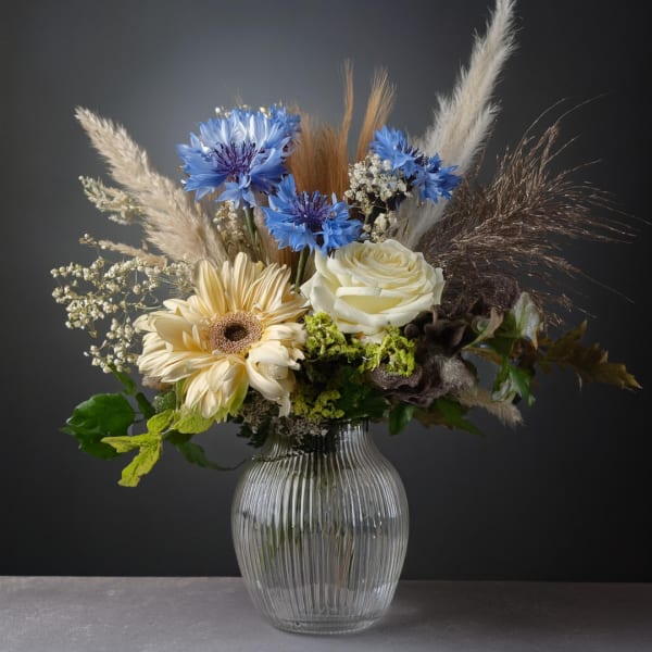 Mixed bouquet with blue and cream flowers in a ribbed glass vase