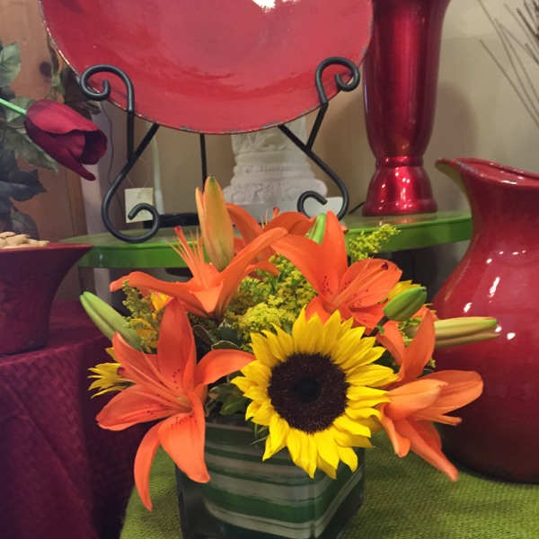 Orange lilies and a sunflower in a square glass vase