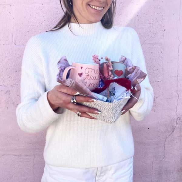 Woman holding a gift basket with two mugs and tissue paper