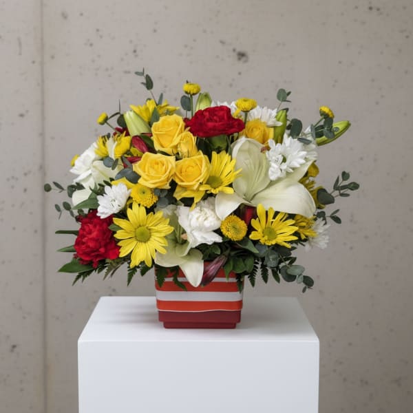 Mixed bouquet of yellow, red, and white flowers in a striped square vase