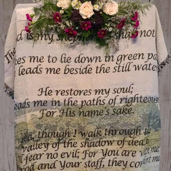 Floral arrangement on a Psalm-printed blanket hanging on a wooden wall
