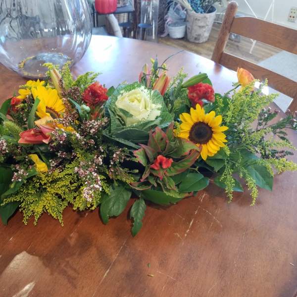 Low floral centerpiece with sunflowers, roses, and lilies on a table