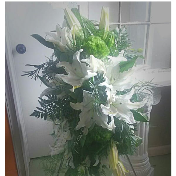 Standing floral spray with white lilies and greenery on a metal easel