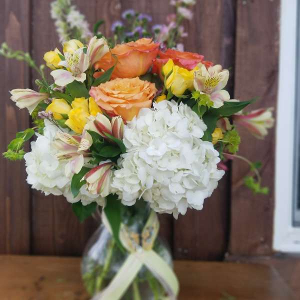 Bouquet of orange and yellow roses with white hydrangeas in a glass vase
