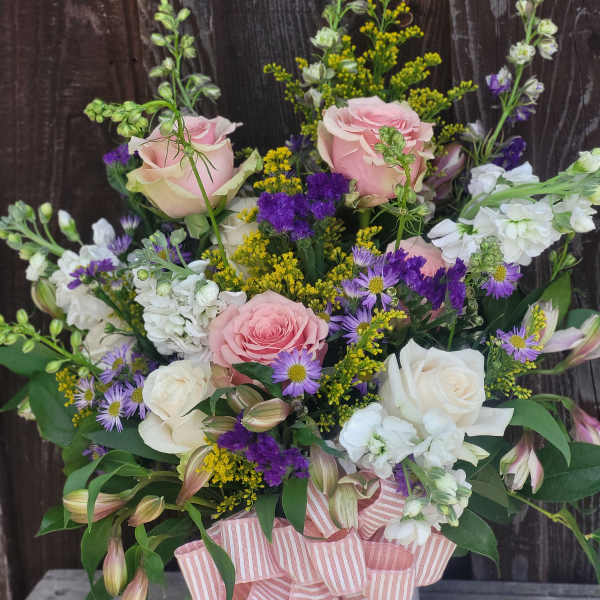 Pink and white roses with purple filler flowers in a white hatbox