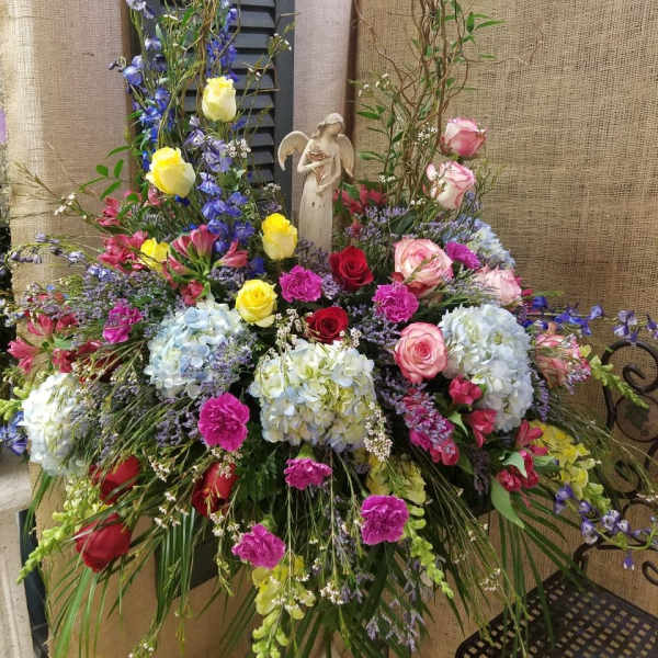 Large mixed floral arrangement with roses, hydrangeas, and an angel figurine