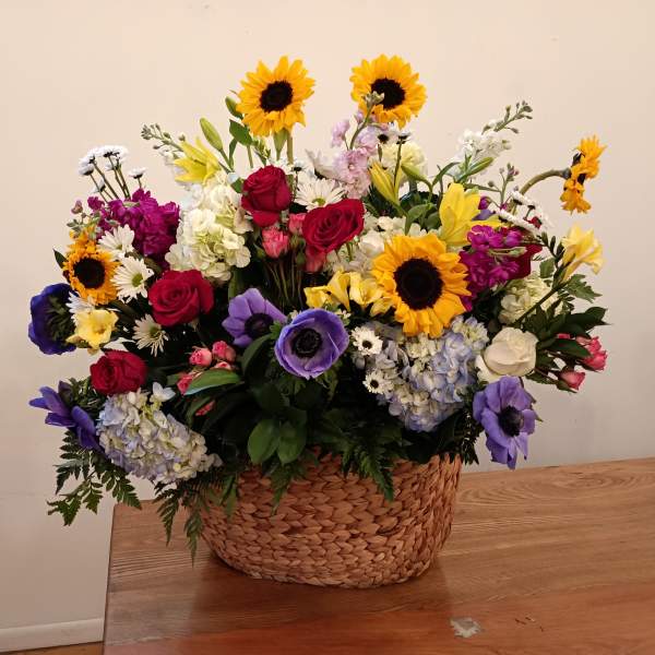 Mixed bouquet in a woven basket with sunflowers, roses, and purple blooms