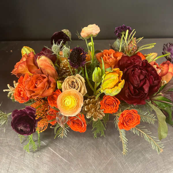 Low floral arrangement with orange, burgundy, and peach blooms