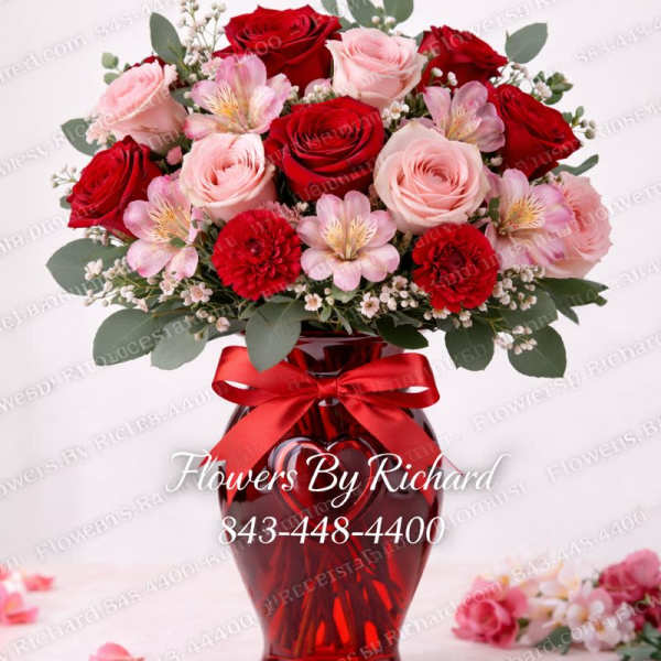 Red and pink roses arranged in a red glass vase with a ribbon.