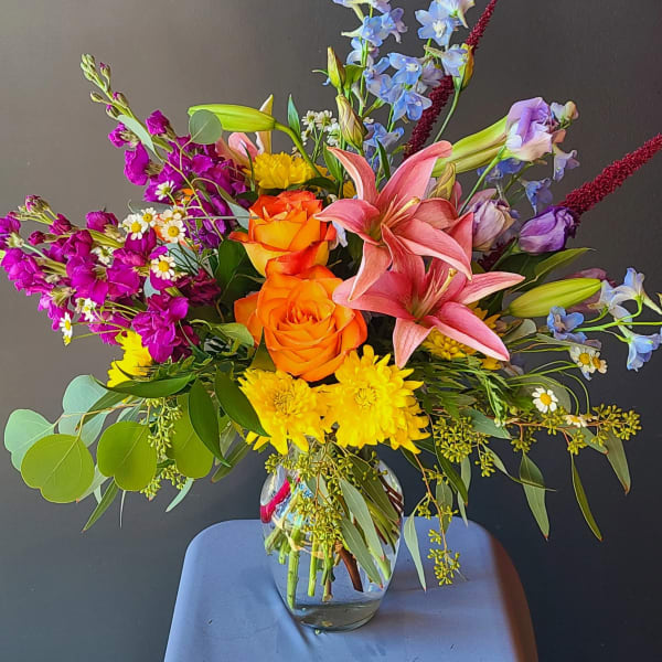 Mixed bouquet of orange roses, pink lilies, and purple flowers in a glass vase