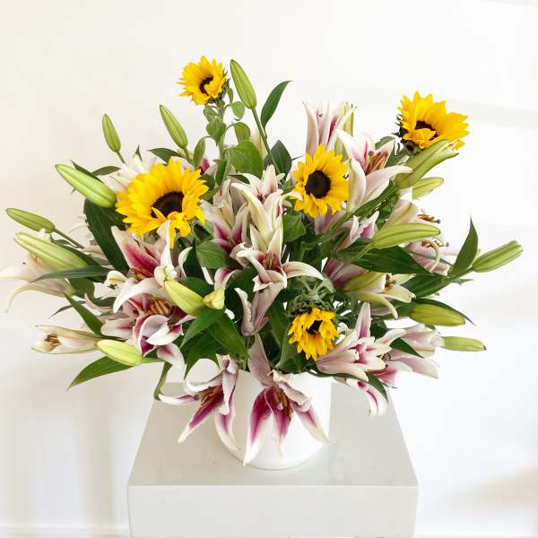 Bouquet of white-and-pink lilies with yellow sunflowers in a white vase