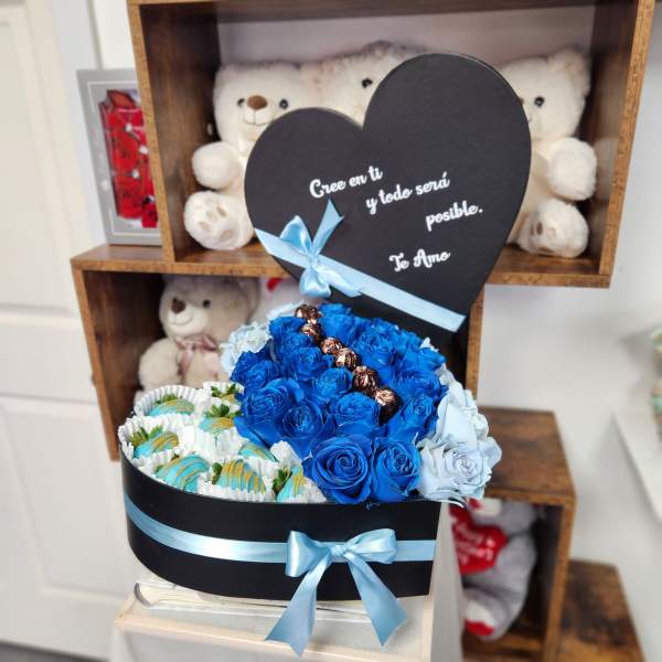 Blue roses and chocolates in a black heart-shaped box with a teddy bear
