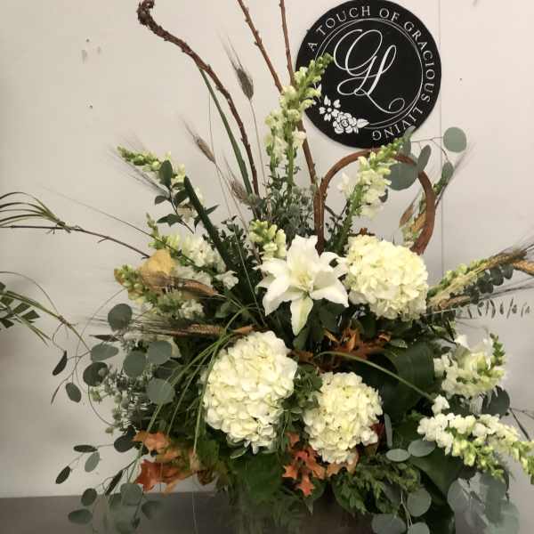 Tall floral arrangement with white lilies and pale hydrangeas in a basket