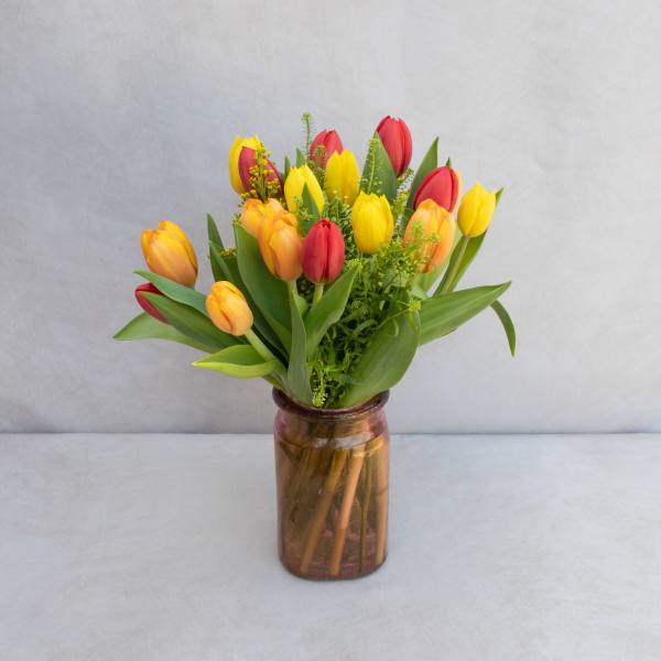 Bouquet of red, yellow, and orange tulips in a brown glass vase