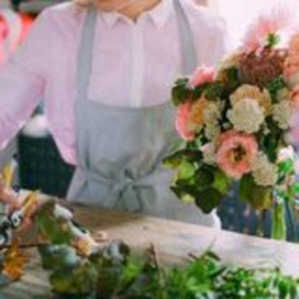 Person in an apron arranging pink and white flowers in a vase.