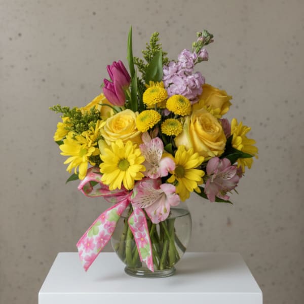 Mixed bouquet of yellow and pink flowers in a glass vase with a patterned ribbon