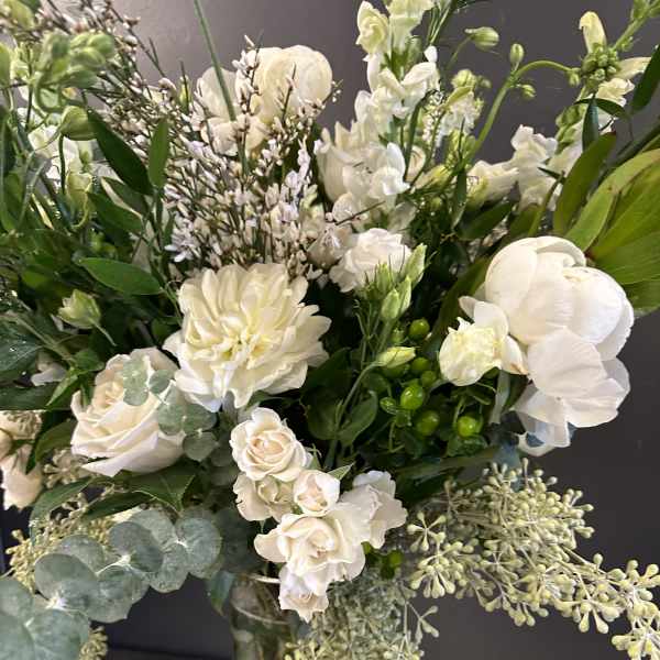 White floral bouquet in a clear glass vase with mixed greenery