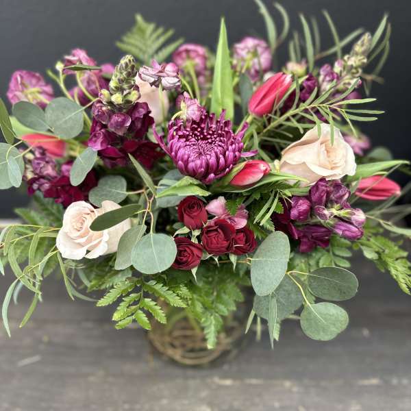 Mixed bouquet of pink and burgundy flowers in a basket vase