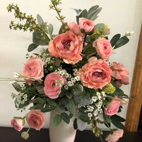 Pink ranunculus bouquet in a white vase with small white filler flowers