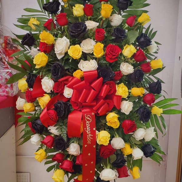Large standing rose arrangement in red, yellow, white, and black with a red bow