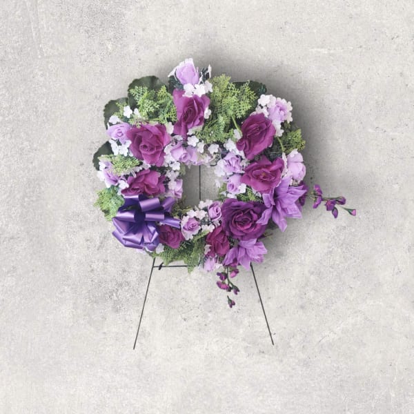 Purple floral wreath with a ribbon bow on a metal stand