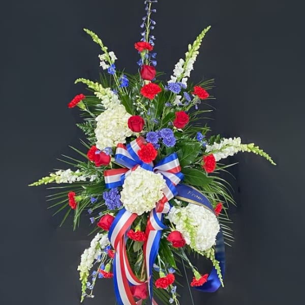 Standing floral spray with red roses, white hydrangeas, and blue accents
