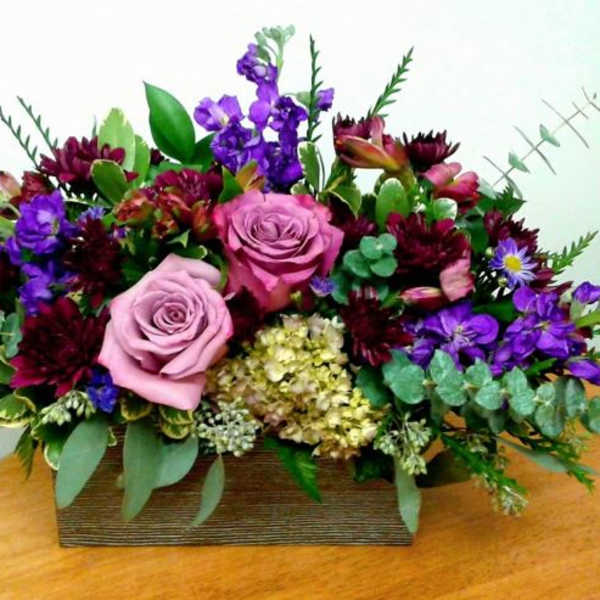 Mixed bouquet with pink roses and purple flowers in a rectangular wooden container