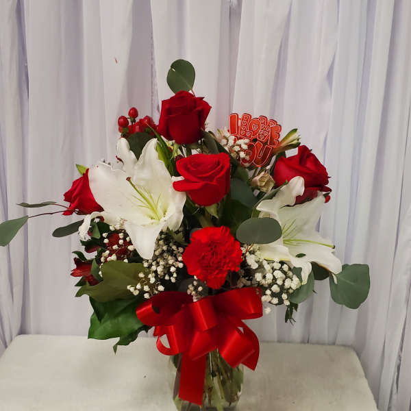 Red roses and white lilies in a glass vase with a red ribbon