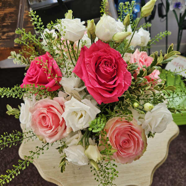 Arrangement of bright pink and peach roses with white lisianthus on a small table