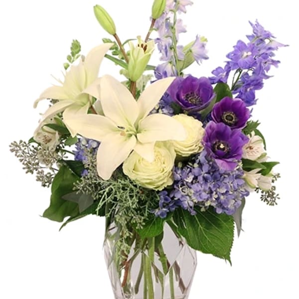 Bouquet of white lilies and purple flowers in a clear glass vase