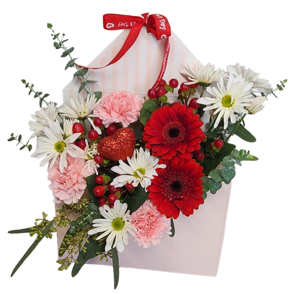 Envelope-shaped pink box filled with red gerbera daisies, white daisies, pink carnations, and a red glitter heart pick.