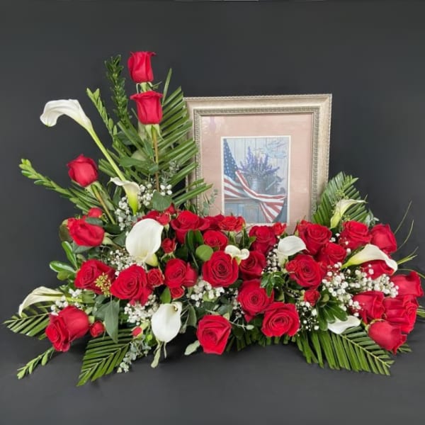 Red roses and white calla lilies arranged around a framed picture.