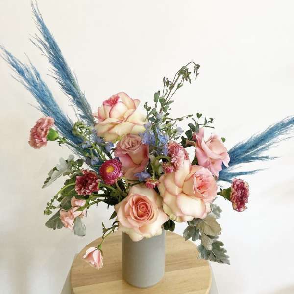 Pink and cream roses arranged in a gray vase with blue pampas grass