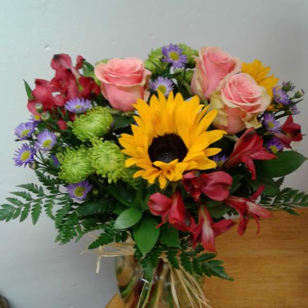 Bouquet of pink roses, a sunflower, and mixed blooms in a glass vase
