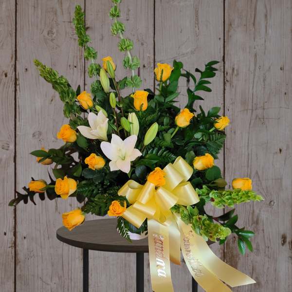 Yellow roses and white lilies in a vase with a yellow ribbon