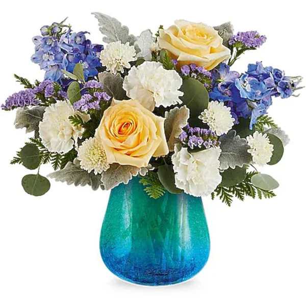 Bouquet of yellow roses, blue flowers, and white blooms in a blue glass vase