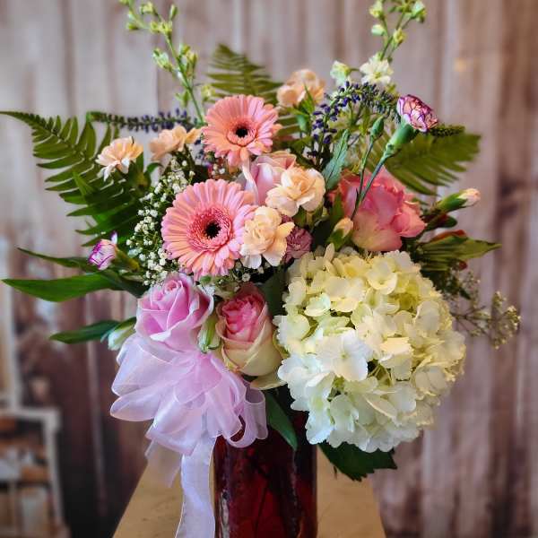 Pink and cream bouquet in a red vase with a lavender ribbon