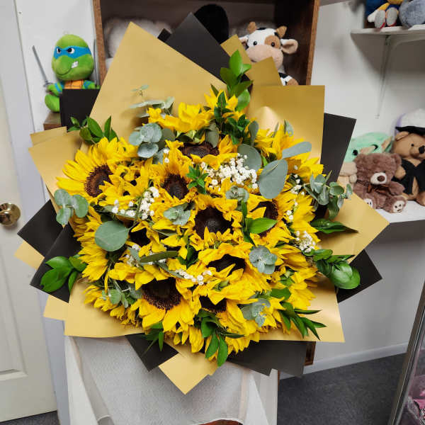 Large bouquet of yellow sunflowers with greenery and black-and-gold wrap