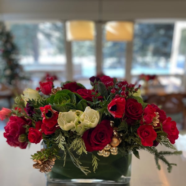 Red and white roses arranged in a low glass vase with holiday accents