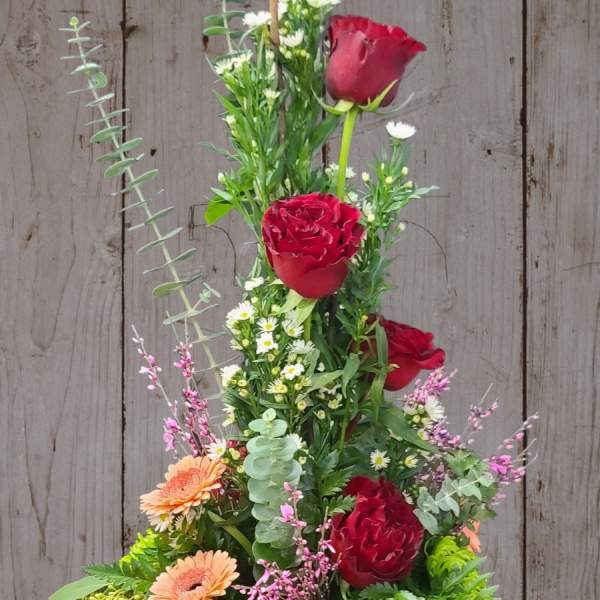 Tall floral arrangement with red roses, peach daisies, and pink berries in a vase