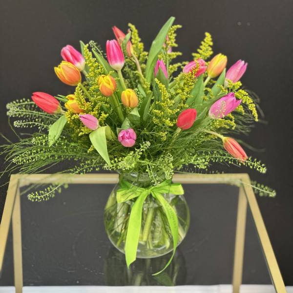 Colorful tulip bouquet in a round glass vase with a green ribbon