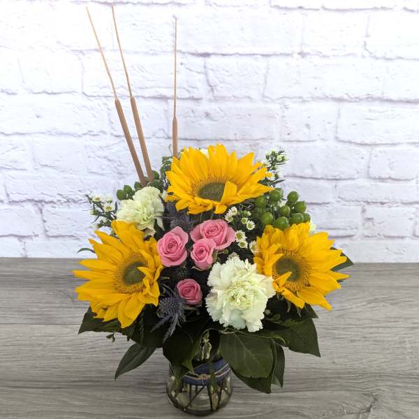 Bouquet of sunflowers, pink roses, and white carnations in a glass vase