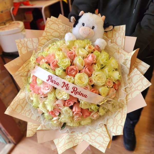 Bouquet of pink and pale yellow roses with a plush cow topper