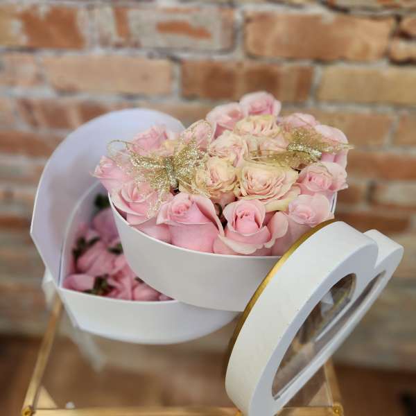 Pink and cream roses in a white heart-shaped box with gold bows