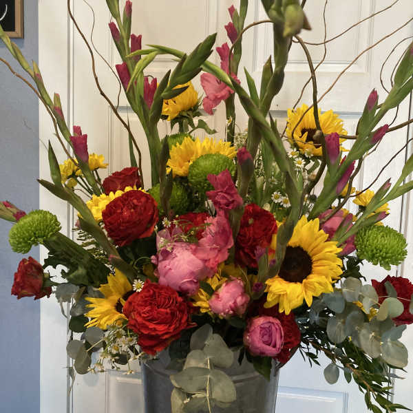 Tall mixed bouquet in a metal vase with sunflowers, red roses, and pink blooms