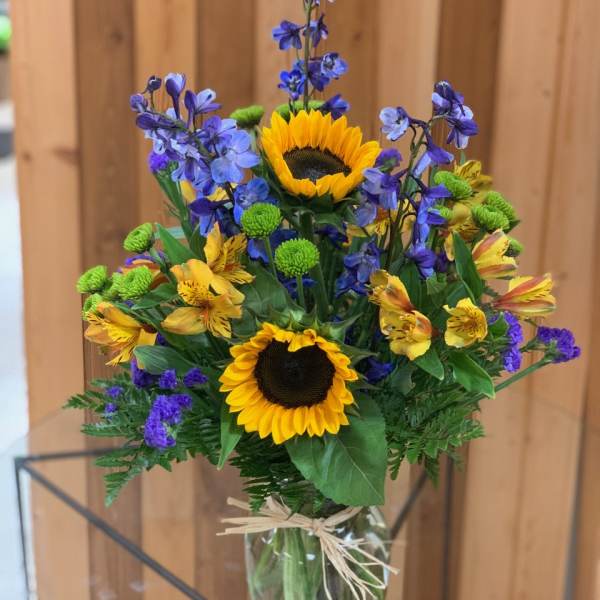 Bouquet of sunflowers, blue flowers, and yellow alstroemeria in a glass vase