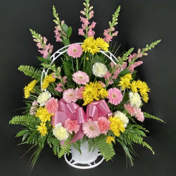 Pink and yellow mixed flower arrangement in a white basket with a pink bow